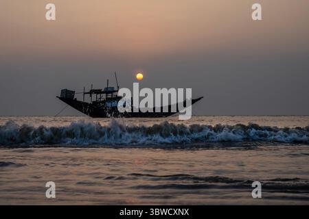 Traditionelles hölzernes Fischerboot mit einer Silhouette vor einem ruhigen Hintergrund des Ozeans während des Sonnenuntergangs. Stockfoto