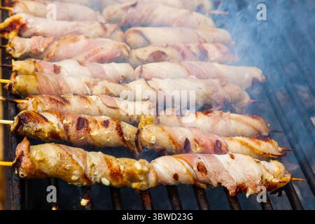 Fleisch, das mit Speck auf Holzspießen gewickelt ist, wird gegrillt. Stockfoto