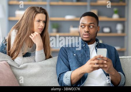 Untreue-Konzept. Verdächtige Junge Frau, Die Ihren Schwarzen Freund Beim Telefonieren Beobachtet Stockfoto