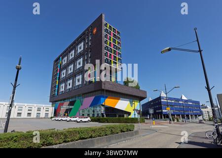 Ein beeindruckendes modernes Doornroosje-Gebäude mit einer farbenfrohen, abstrakten Fassade und rechteckigen Fenstermustern, das unter einem klaren blauen Himmel in Nijmegen steht. Stockfoto