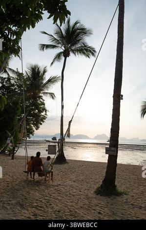 Ein Elternteil mit zwei Kindern auf einer Schaukel, der den Sonnenaufgang am frühen Morgen im Paradise Koh Yao, einem Boutique-Resort im Nordosten der insel, beobachten kann Stockfoto