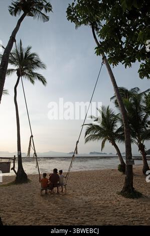 Ein Elternteil mit zwei Kindern auf einer Schaukel, der den Sonnenaufgang am frühen Morgen im Paradise Koh Yao, einem Boutique-Resort im Nordosten der insel, beobachten kann Stockfoto