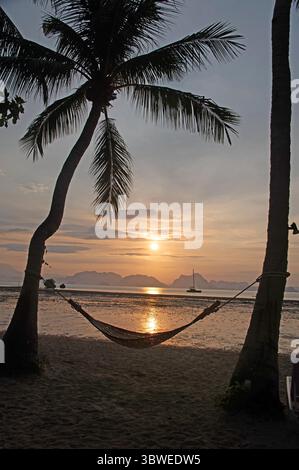 Eine Silhouette des frühen Sonnenaufgangs mit einer Hängematte, die von ein paar Kokospalmen am Strand von Paradise Koh Yao, einer Boutique, gestützt wird Stockfoto