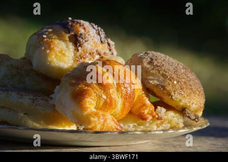 Frisch gebackenes argentinisches Gebäck, einschließlich Croissants und Muffins, auf einem Teller, im Sonnenlicht gebadet Stockfoto