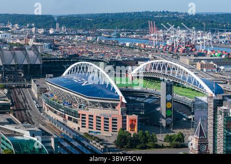 Seattle, Vereinigte Staaten - 25. Mai 2023: Aus der Vogelperspektive ein pulsierendes Stadion inmitten einer weitläufigen Stadtlandschaft, im Kontrast zum Industriehafen mit hoch aufragenden Kränen und weit entfernten, üppigen Hügeln. Stockfoto