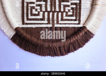 Geometrische Wandkunst in Braun und weiß aus Makramee Eine handgefertigte Makramee-Wand mit geometrischem braunem und weißem Muster, die präzise gewebt wurde. Stockfoto