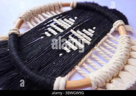 Elegante Wandaufhängung in Schwarz und weiß aus Makramee. Eine atemberaubende schwarz-weiße Makramee-Wand mit komplizierten gewebten Mustern und einem Holzkorb Stockfoto