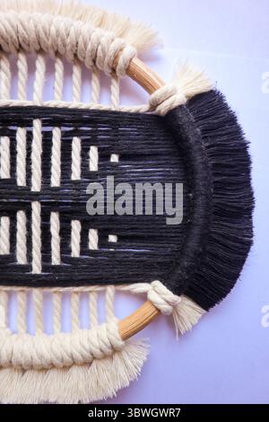 Elegante Wandaufhängung in Schwarz und weiß aus Makramee. Eine atemberaubende schwarz-weiße Makramee-Wand mit komplizierten gewebten Mustern und einem Holzkorb Stockfoto