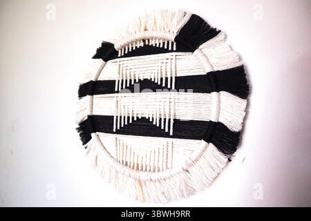 Handgewebte runde Wandaufhängung in Schwarz und weiß. Eine handgefertigte, gewebte Wandkunst in einem auffälligen Schwarz-weiß-Muster. Das geometrische Design und die Fransen-Detai Stockfoto
