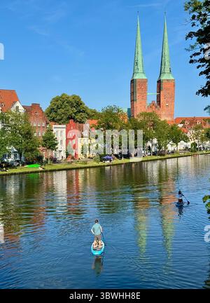 Die Besucher paddeln auf der Trave in Lübeck, Deutschland, mit den berühmten Doppeltürmen der Marienkirche und historischen Gebäuden entlang des Wassers Stockfoto