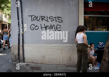 Leute, die neben einem Graffiti an einer Mauer im Stadtzentrum gesehen wurden, mit der Aufschrift "Touristen gehen nach Hause". Mit mehr als 18 Millionen Touristen, die 2024 Barcelona besuchen werden, hat die Stadt Schwierigkeiten, ein Gleichgewicht zwischen den wirtschaftlichen Vorteilen des Tourismus während der Tourismussaison und der Notwendigkeit zu finden, die Stadt für die Einwohner lebenswert zu halten, die dem Massentourismus und der Ausbeutung der Stadt durch die Tourismusbranche zunehmend feindlich gegenüberstehen. Stockfoto