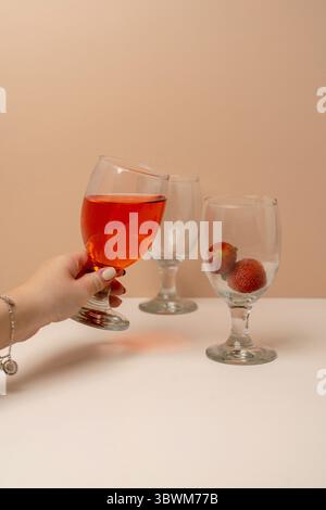 Die Hand der Frau hält ein Glas Erdbeerwein oder Saft. Eine Szene des Feierns, der Verkostung oder einer Party. Cheers-Konzept. Stockfoto