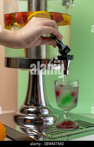 Gießen von mit Obst angereichertem Wasser aus einem Getränkespender. Erfrischendes Entgiftungswasser mit Erdbeere und Zitrone, serviert in einem Vintage-Glas. Stockfoto