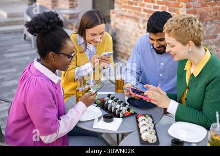 Freunde, die Sushi teilen und Telefone verwenden Stockfoto