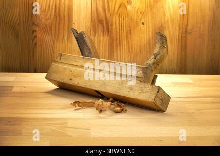 Handflugzeug aus Vintage-Holzverarbeitung auf einer sauberen Holzoberfläche, hervorgehoben durch warme Deckenbeleuchtung, mit Spänen, die handwerkliches Können darstellen, TRA Stockfoto
