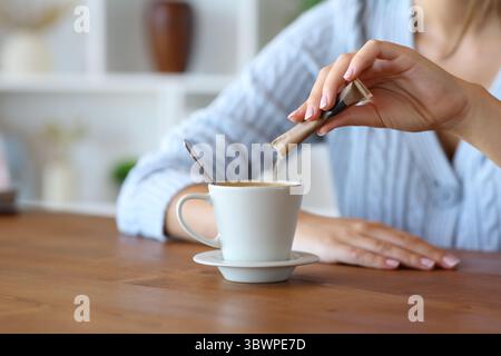Nahaufnahme einer Frauenhand, die Zucker zu Hause in den Kaffee eingießt Stockfoto
