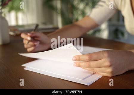Nahaufnahme einer Frau, die zu Hause ein Dokument auf einem Holztisch hält und liest Stockfoto