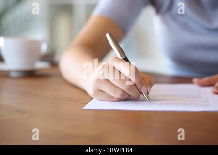 Nahaufnahme einer Frau, die zu Hause auf einem Holztisch auf Papier schreibt Stockfoto