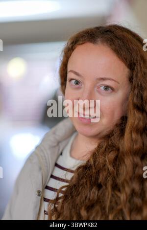 Eine fröhliche junge Frau mit lockigem Haar genießt ihre Zeit bei einer freundlichen Indoor-Veranstaltung. Stockfoto
