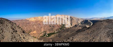 Panoramablick auf die zerklüfteten Wüstenberge in der Nähe von Dhiban, Madaba Governorate, Jordanien, mit gewundenen Straßen und tiefem Tal unter klarem blauem Himmel. Stockfoto