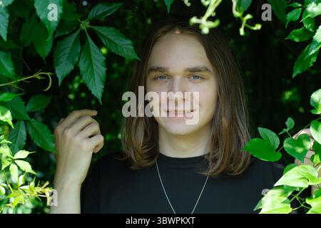 Ein junger Mann steht umgeben von leuchtend grünen Blättern und lächelt hell in der Natur. Stockfoto