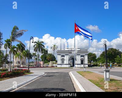 Eintritt zum Santa Ifigenia Friedhof in Santiago de Cuba, mit kubanischer Flagge, die unter blauem Himmel winkt – ein nationaler Ort der Erinnerung und der Ruhe der Helden Stockfoto