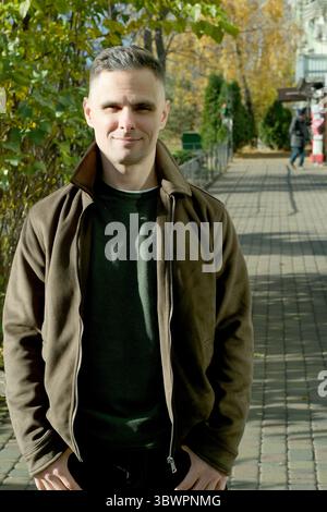 Ein fröhliches Individuum steht auf einem gemauerten Weg, umgeben von bunten Herbstblättern. Stockfoto