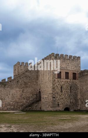 Massive Steinmauern und Turm einer mittelalterlichen Burg stehen hoch vor einem bewölkten Himmel, mit einem grasbewachsenen Innenhof im Vordergrund Stockfoto