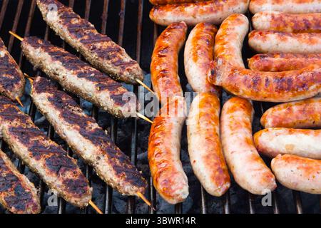 Würstchen und Hackfleisch auf Holzstäbchen werden auf dem Grill gekocht. Stockfoto