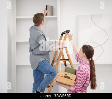 Ein Paar, das Bücher zu Hause mit einer Leiter in die Regale legt Stockfoto