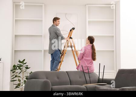 Paare, die zu Hause mit einer Leiter Malerei an die Wand legen Stockfoto
