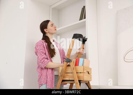 Frau, die zu Hause Bücher in Regale legt, indem sie Leiter benutzt Stockfoto