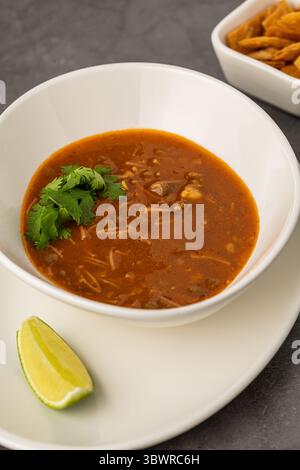 Scharfe mexikanische Hühnersuppe mit Nudeln, garniert mit frischem Koriander und Limettenkeil Stockfoto