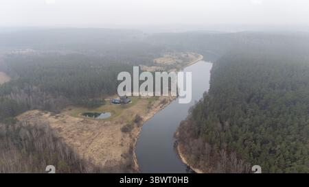 Aus der Vogelperspektive auf einen ruhigen Fluss, der sich durch einen dichten Wald schlängelt, mit einem Haus in der Nähe. Stockfoto