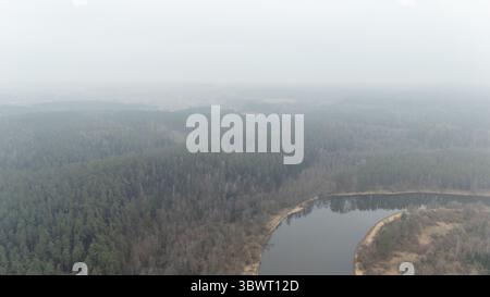 Aus der Vogelperspektive auf eine nebelige Waldlandschaft mit einem ruhigen Fluss, der sich durchzieht. Stockfoto