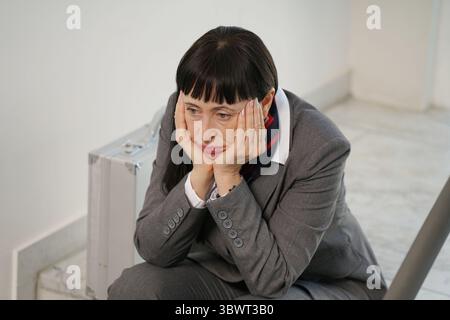 Frau im Anzug sitzt deprimiert auf einer Treppe im Treppenhaus Stockfoto
