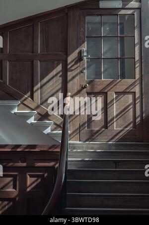 London, Großbritannien - 13. Mai 2025 - Sonnenlicht strömt durch das große Fenster und wirft Licht- und Schattenmuster auf die Oberfläche von Holztüren und Treppen. Sonnenlicht Stockfoto