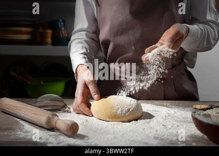 Backkonzept. Kaukasische Frauenhände werfen Mehl auf den Teig. Stockfoto