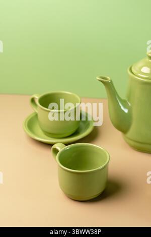 Minimalistisches Teeset aus grüner Keramik. Eine Teekanne, Tasse und Untertasse auf zweifarbigem beigem und pastellgrünem Hintergrund. Stillleben mit Kopierraum. Stockfoto