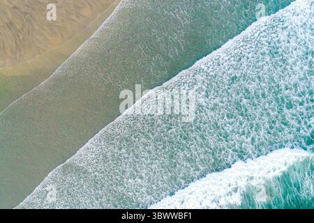 Luftaufnahme der schäumenden Wellen des Ozeans, die auf einem Sandstrand zusammenbrechen, Luftdrohne von oben nach unten, zenithal Stockfoto