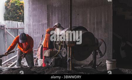 Bauarbeiter mischen Baumaterialien wie Zement, Sand und Wasser, um eine starke Mischung zu schaffen, die für eine dauerhafte und effektive Konstruktion unerlässlich ist Stockfoto