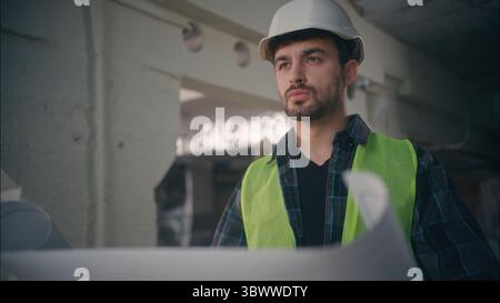 Seriöser kaukasischer Bauunternehmer Handwerker Architekt-Arbeiter-Blick Baumeister Werkarbeiter Baumeister Ingenieur hält Bauentwurf im Bau männlich Stockfoto
