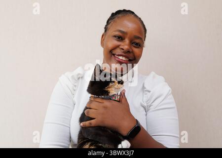 Nahaufnahme Porträt, junge schwarze afroamerikanerin, die zu Hause eine niedliche Tabbykatze hält und streichelt. Positive Menschen, emotional in Liebe zu Tiertier, fac Stockfoto