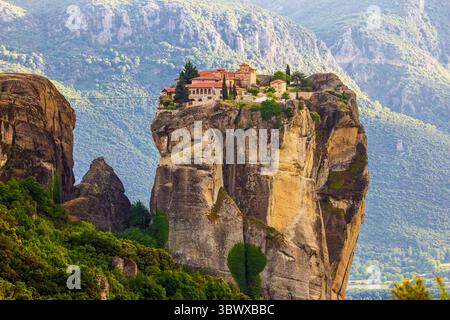 Nachmittagssommerblick auf die Meteora-Landschaft in Griechenland, mit dem Kloster der Heiligen Dreifaltigkeit, das auf einer dramatischen monolithischen Felsformation in Th thront Stockfoto