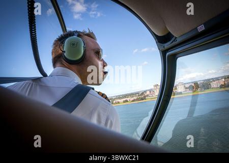 Hubschrauberpilot in einem Robinson R44 Hubschrauber, der aus dem Seitenfenster blickt, während er während des Fluges das offene Wasser umdreht. Stockfoto