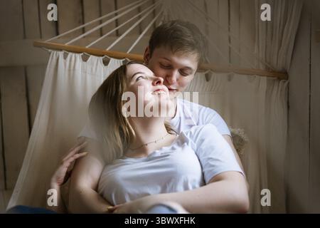 Porträt eines jungen schönen Paares, eines jungen Erwachsenen Mannes und einer Frau in einer Hängematte. Die Frau ist eine attraktive Blondine, der Mann ist dunkelhaarig in weiß Stockfoto
