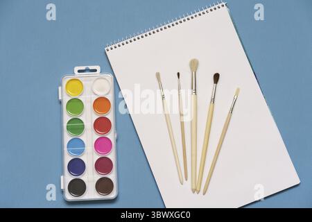 Ein Satz Pinsel, ein Skizzenbuch und helle Aquarelle auf blauem Hintergrund. Das Konzept der Kreativität Stockfoto