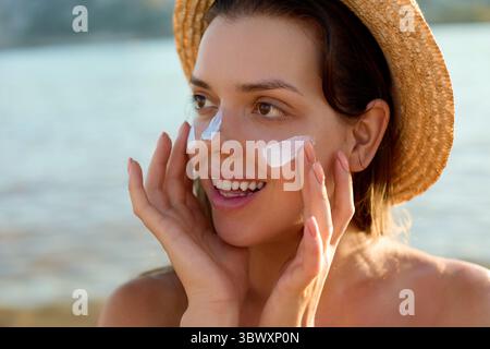 Sonnencreme-Frau, die Sonnencreme aufträgt. Schöne glückliche, süße Frau, die Sonnencreme auf ihre Nase aufträgt. Stockfoto