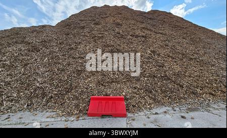 Massiver Haufen Holzspäne mit roter Barriere und blauem Himmel Stockfoto