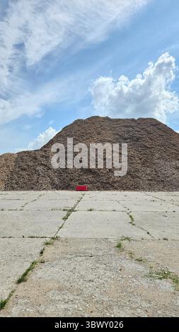 Massiver Haufen Holzspäne mit roter Barriere und blauem Himmel Stockfoto